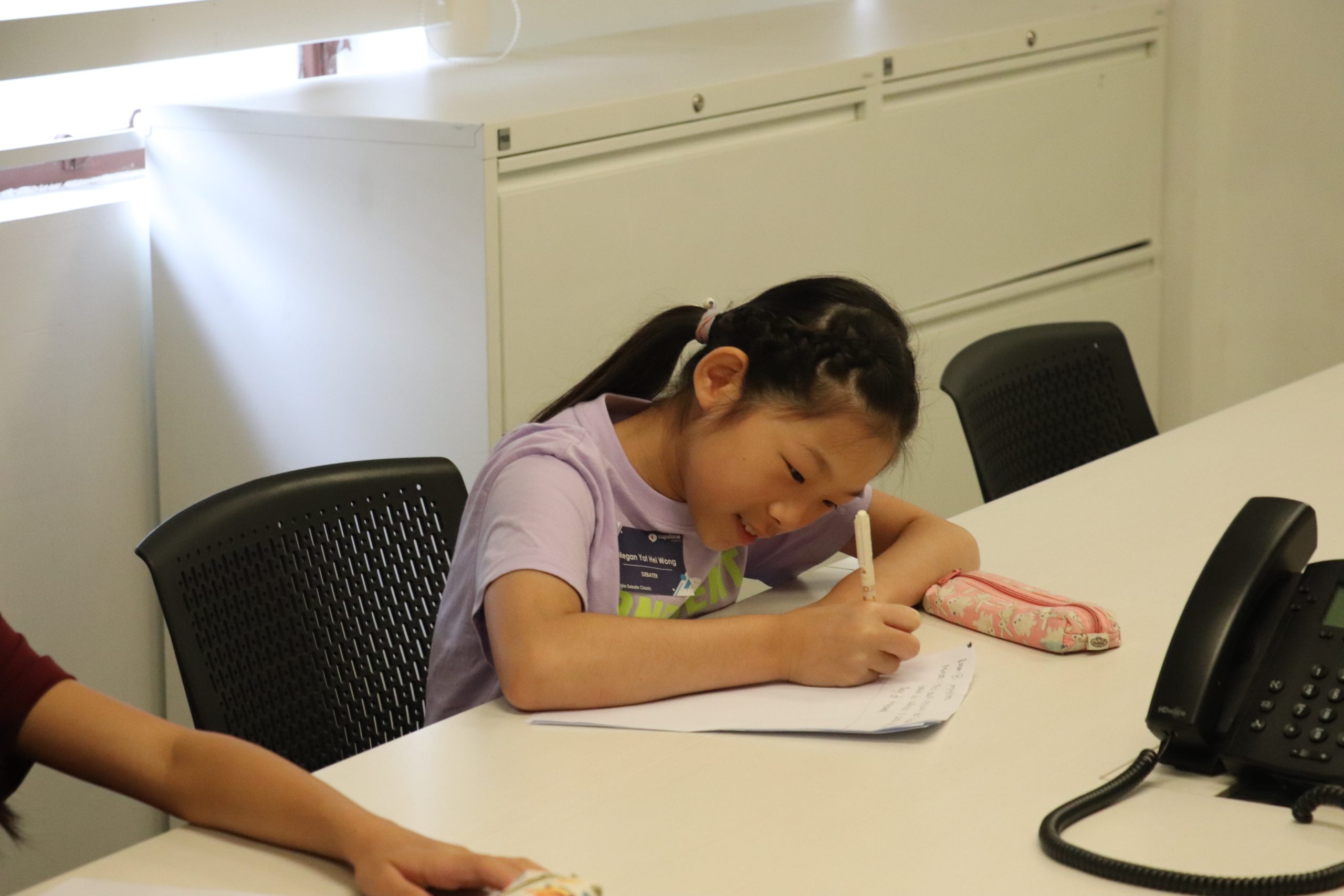 Primary-aged student writes notes during a Capstone speaking class