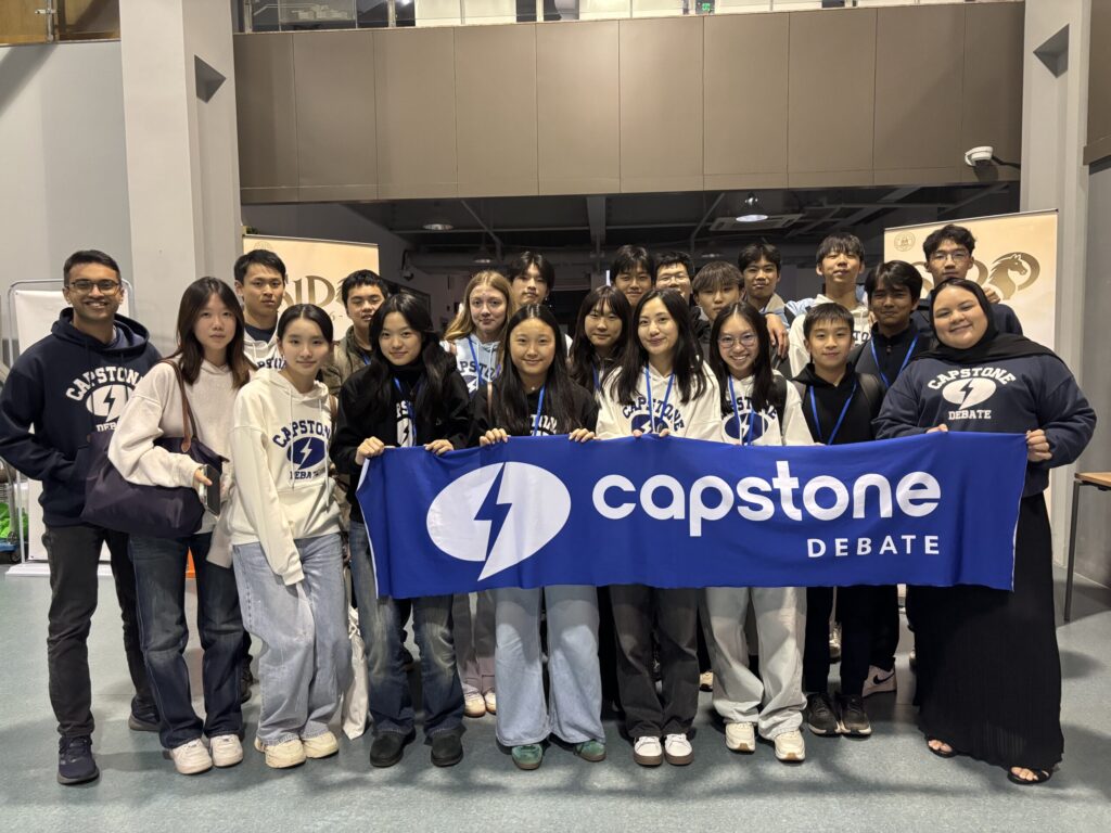 Group of Capstone Debate students and coaches holding a banner indoors